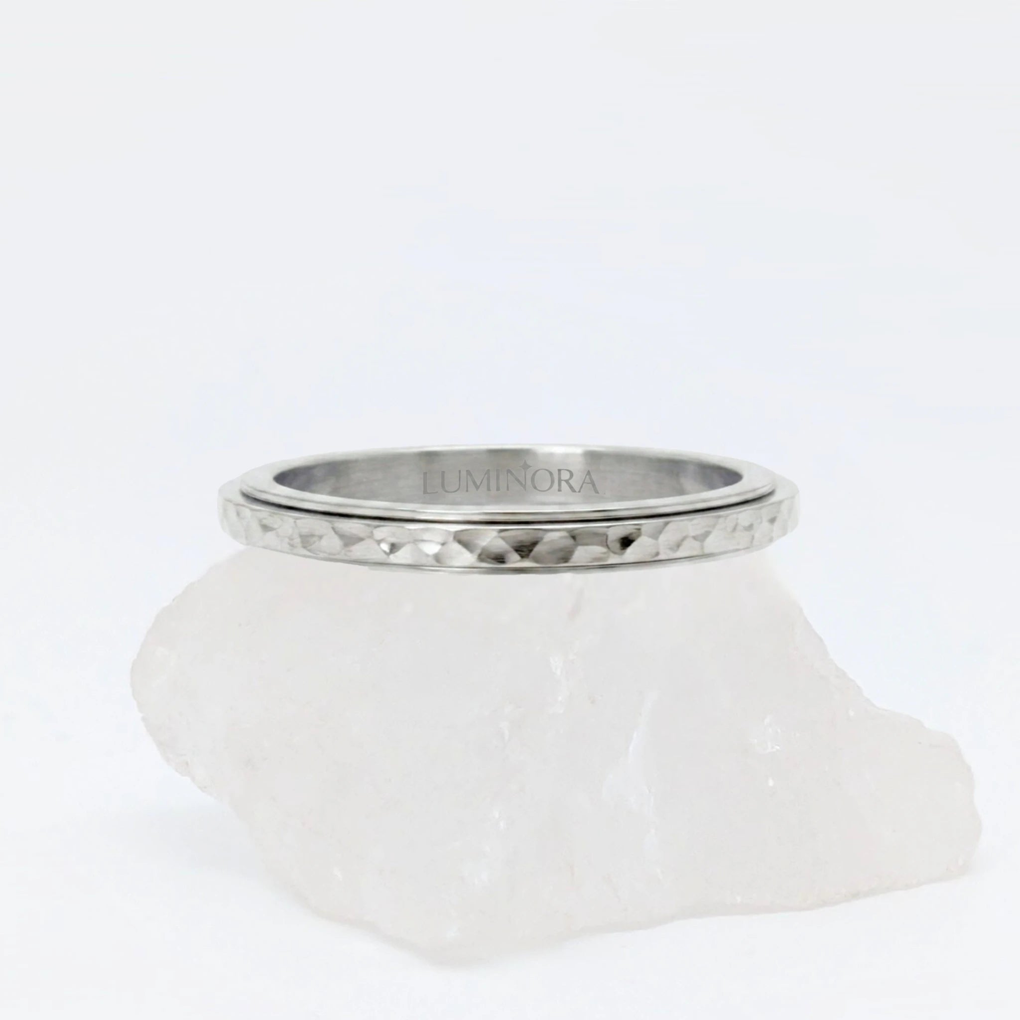 Zilveren Luna anxiety ring ontworpen met een elegant gehamerd oppervlak, geplaatst op een witte kwartssteen.
