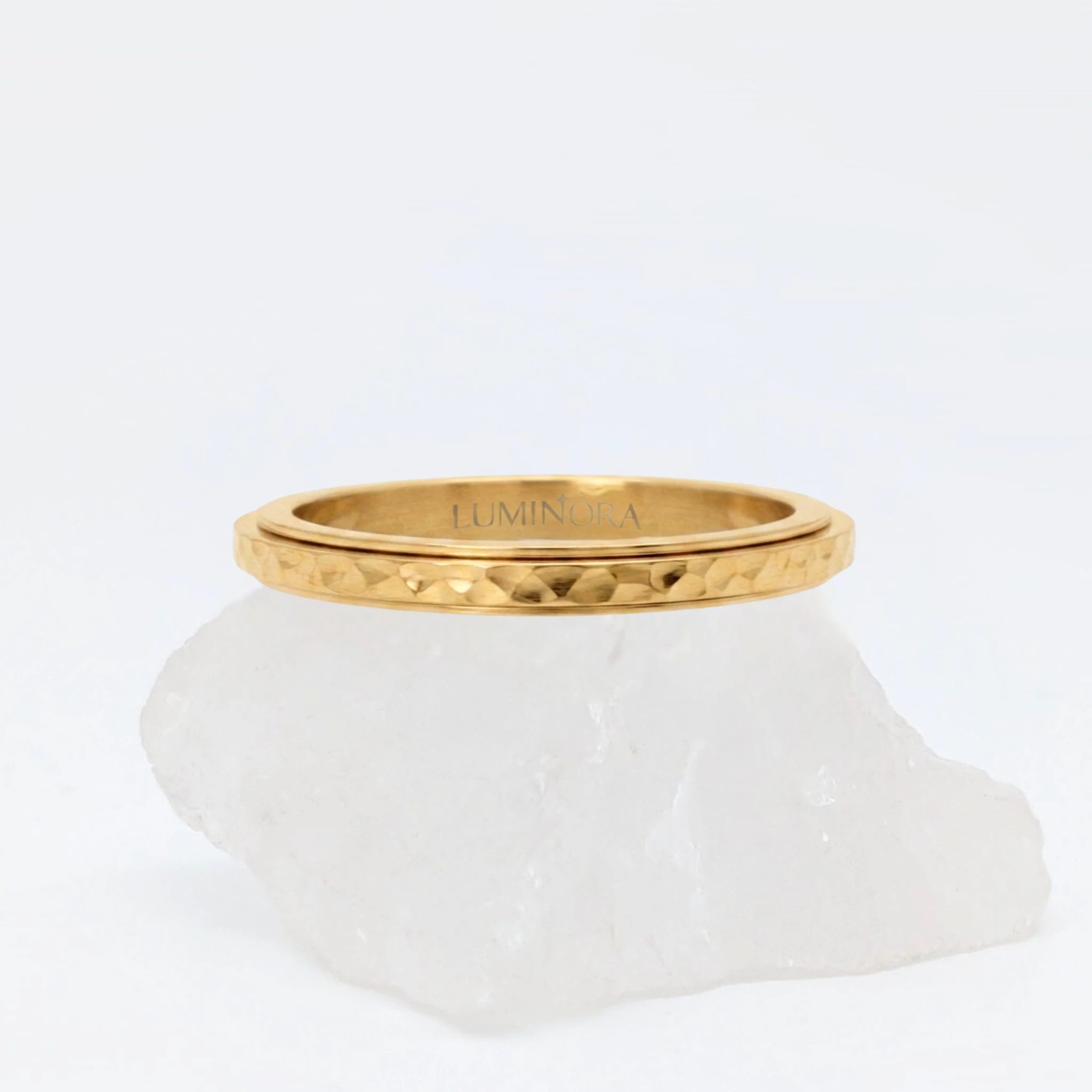 Gouden Luna fidget ring met een unieke gehamerde textuur die het licht prachtig weerkaatst, gepresenteerd op een witte steen.