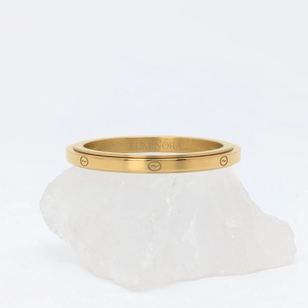 Gouden Marea fidget ring met een glad oppervlak en verfijnde gegraveerde golfjes, gepresenteerd op een witte steen.