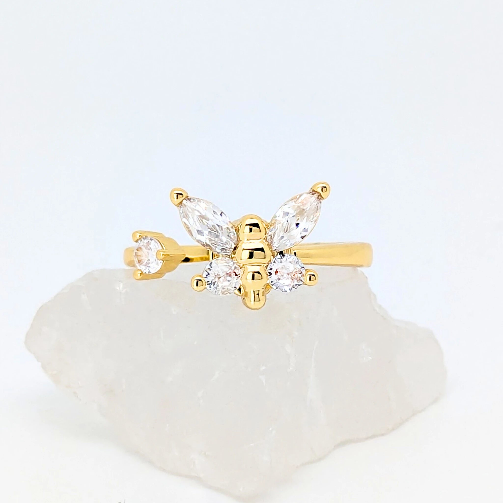 Gouden Nabi fidget ring met een elegante sprankelende vlinder liggend op een witte ruwe steen.