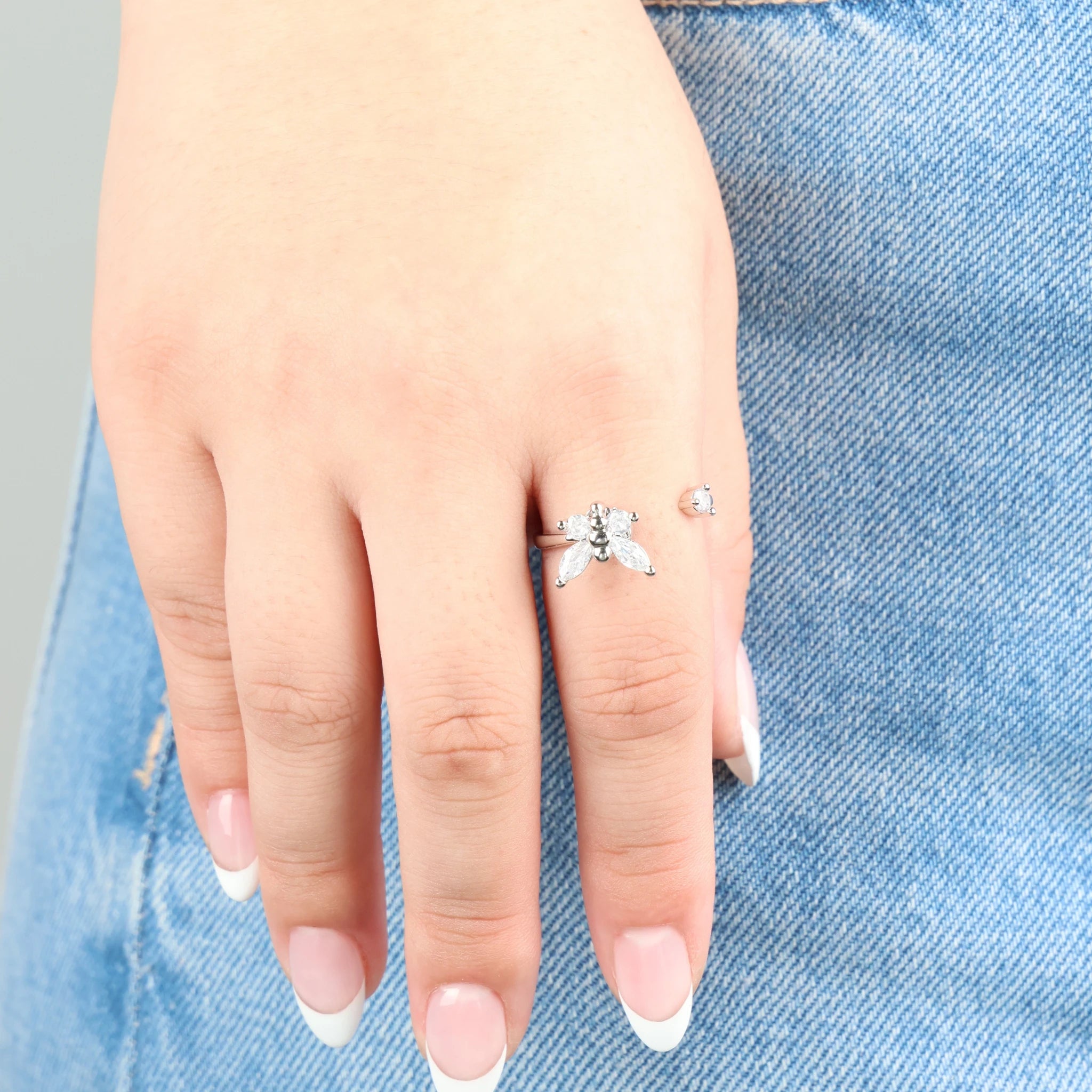 Close-up van de zilveren Nabi stress ring met vlinderontwerp gedragen op een jeans.
