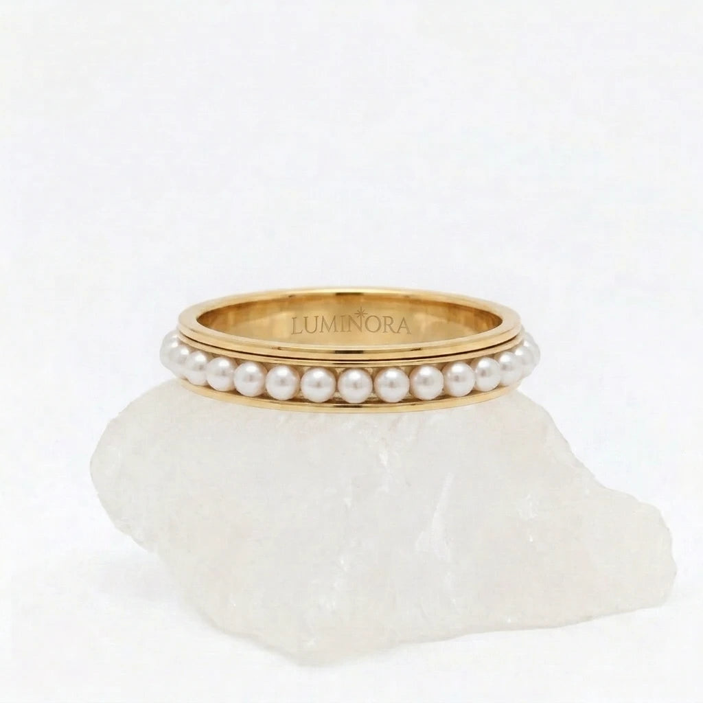 Gouden Perla fidget ring van RVS met een draaiende band van witte parels, gepresenteerd op een witte steen. 
