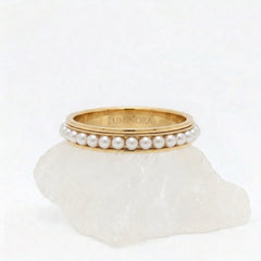 Gouden Perla fidget ring van RVS met een draaiende band van witte parels, gepresenteerd op een witte steen. 