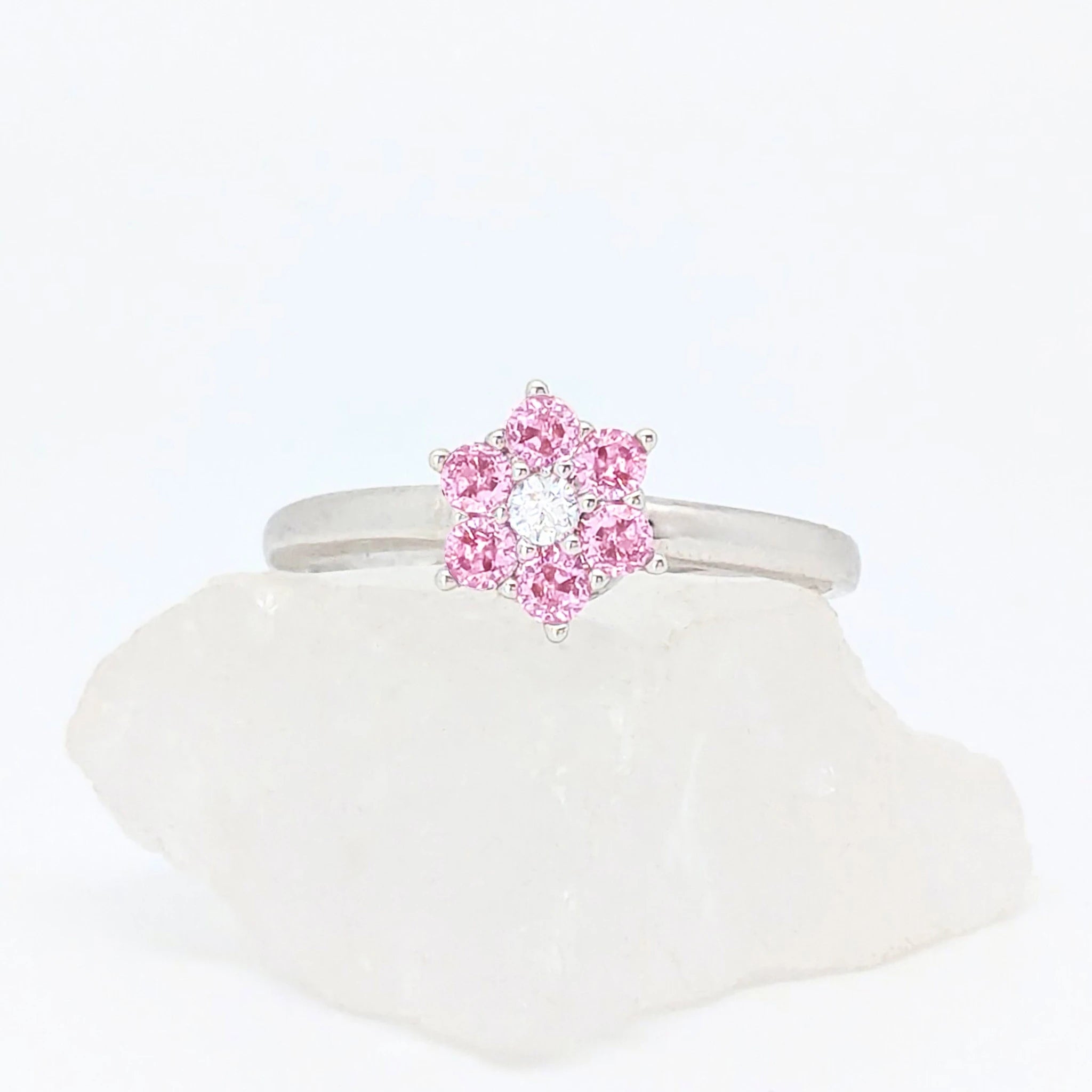 Zilverkleurige Petal fidget ring met een bloemvorm van heldere roze steentjes, gepresenteerd op een witte steen.