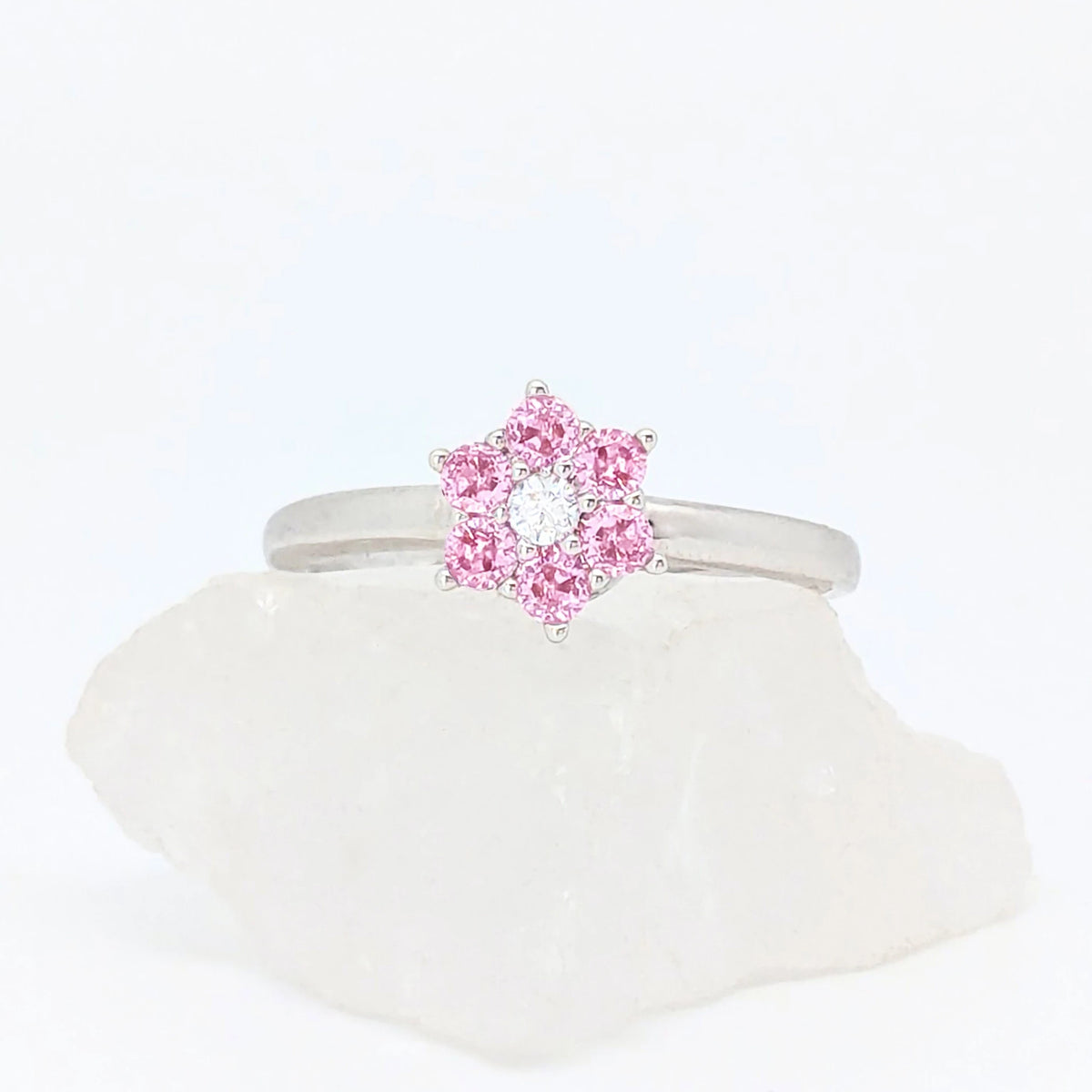 Zilverkleurige Petal fidget ring met een bloemvorm van heldere roze steentjes, gepresenteerd op een witte steen.