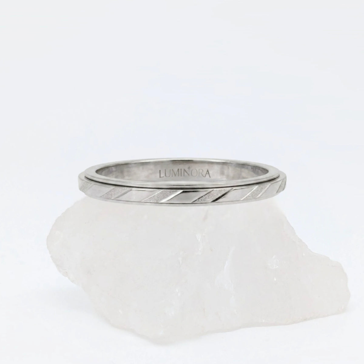 Zilveren Prism anxiety ring met een modern design van diagonale lijnen en facetten, elegant gepresenteerd op een witte steen.