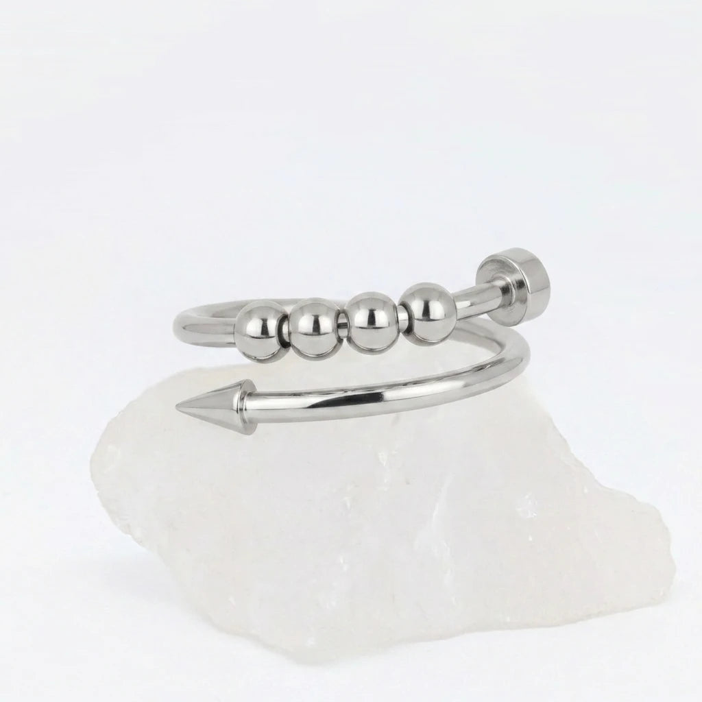 Zilveren Punta Bead fidget ring van RVS in het design van een gebogen spijker met beweegbare kralen, rustend op een witte steen.