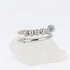 Zilveren Punta Bead fidget ring van RVS in het design van een gebogen spijker met beweegbare kralen, rustend op een witte steen.