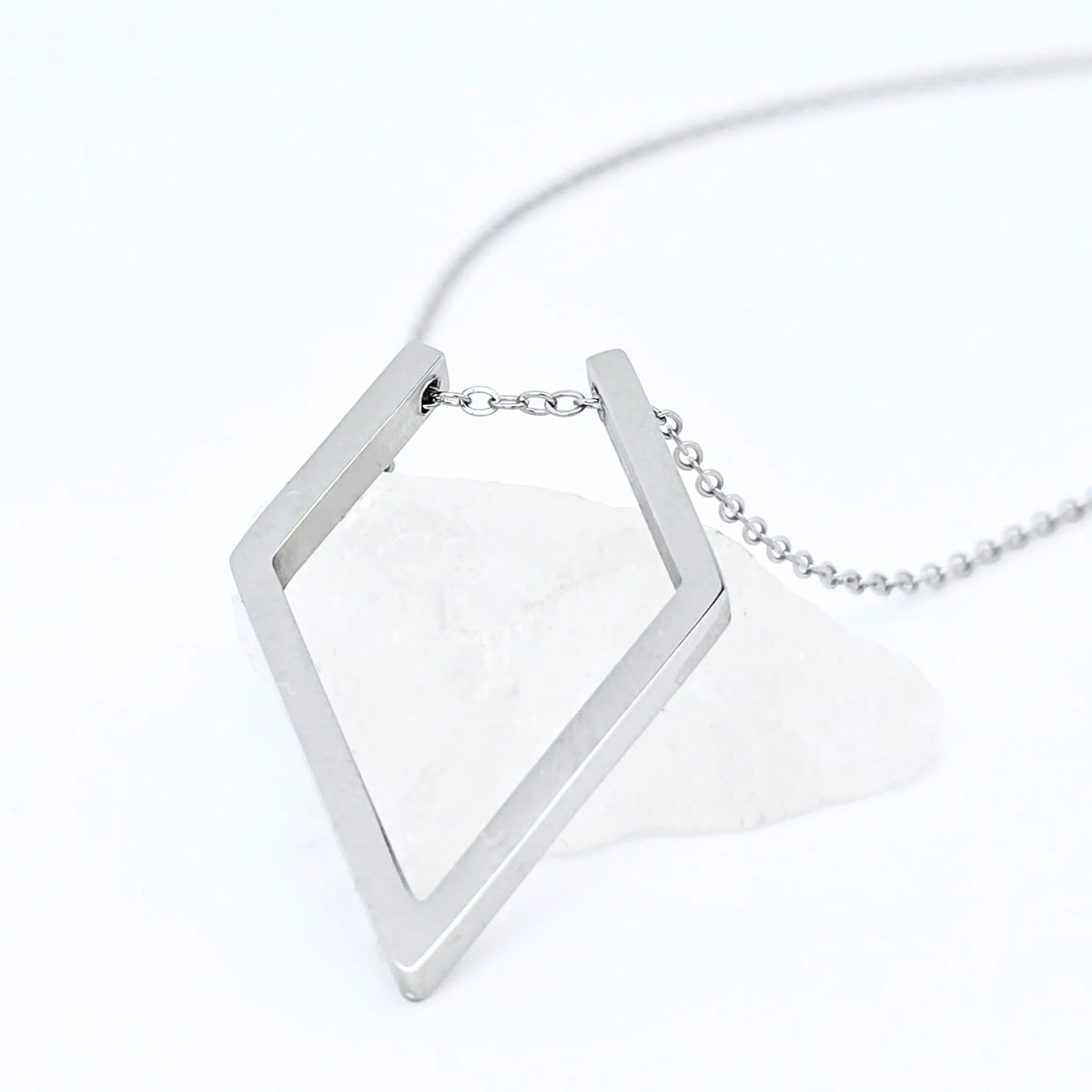 Zilveren Ring Keeper ketting van RVS met een ruitvormige hanger voor ringen, elegant gepresenteerd op een witte steen.