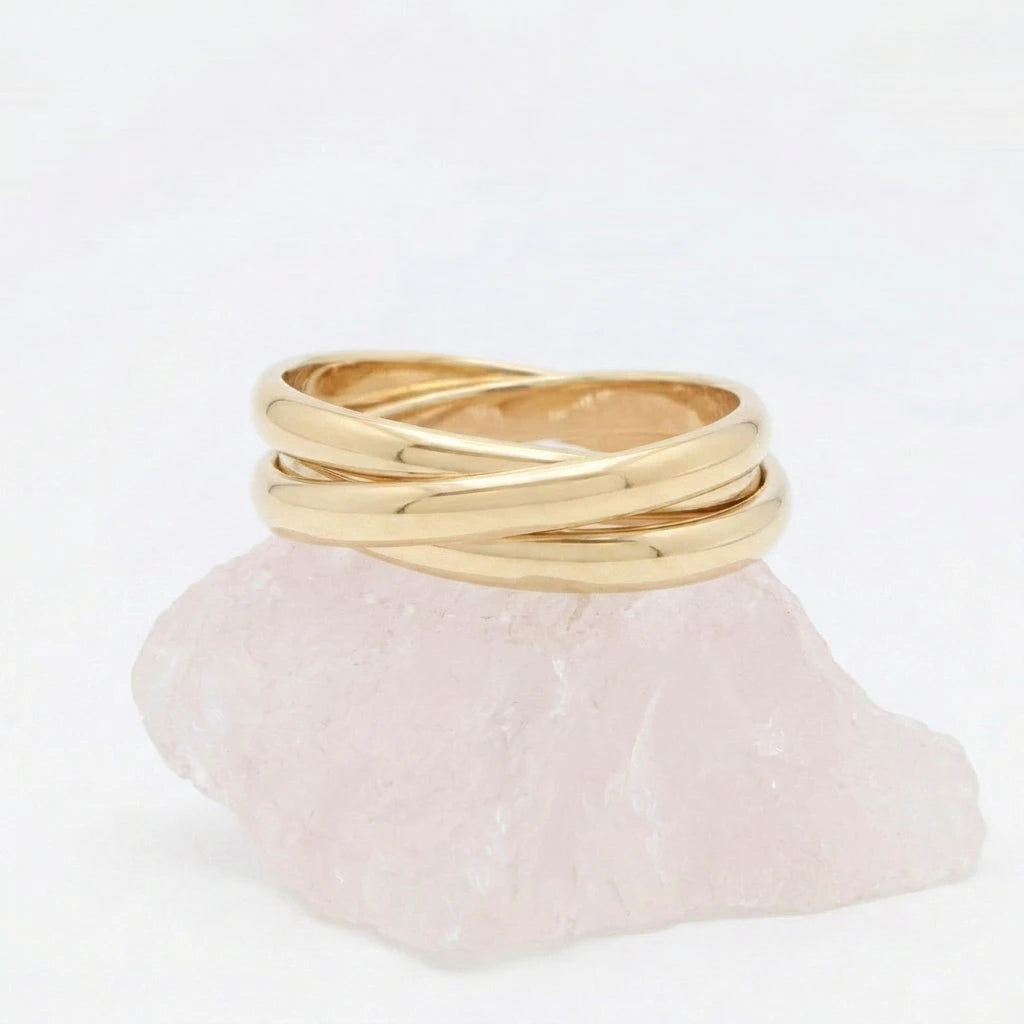 Gouden Trinity fidget ring van RVS opgebouwd uit drie in elkaar vallende, rollende ringen, elegant rustend op een witte steen.