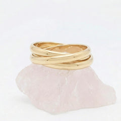 Gouden Trinity fidget ring van RVS opgebouwd uit drie in elkaar vallende, rollende ringen, elegant rustend op een witte steen.