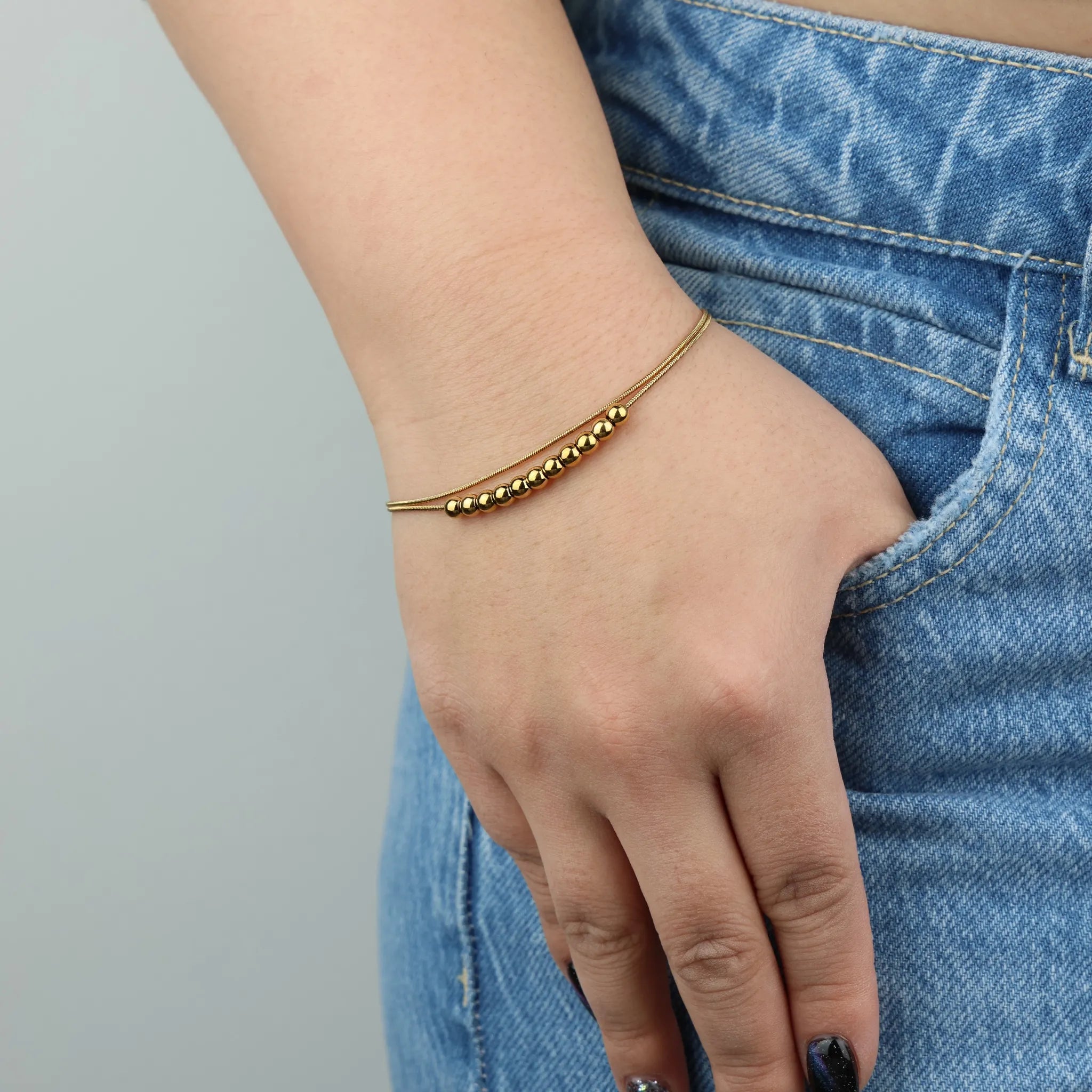 Vrouwenhand draagt goudkleurige Bead fidget armband van RVS bij spijkerbroek – Luminora