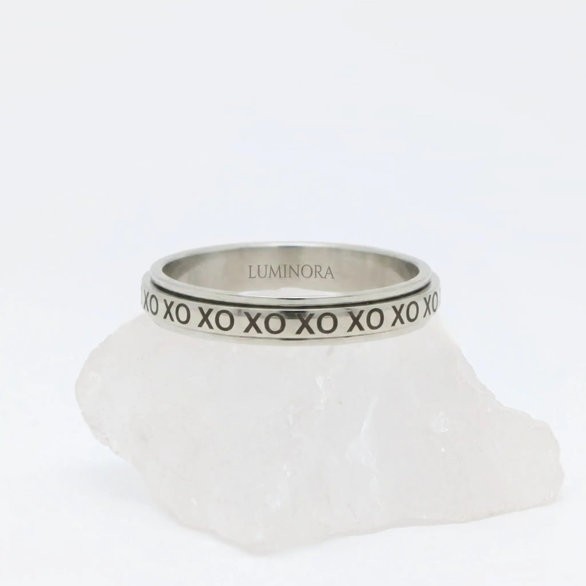 Zilveren XO fidget ring van RVS met een draaibare band voorzien van gegraveerd XO-patroon, gepresenteerd op een witte steen.