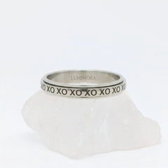 Zilveren XO fidget ring van RVS met een draaibare band voorzien van gegraveerd XO-patroon, gepresenteerd op een witte steen.