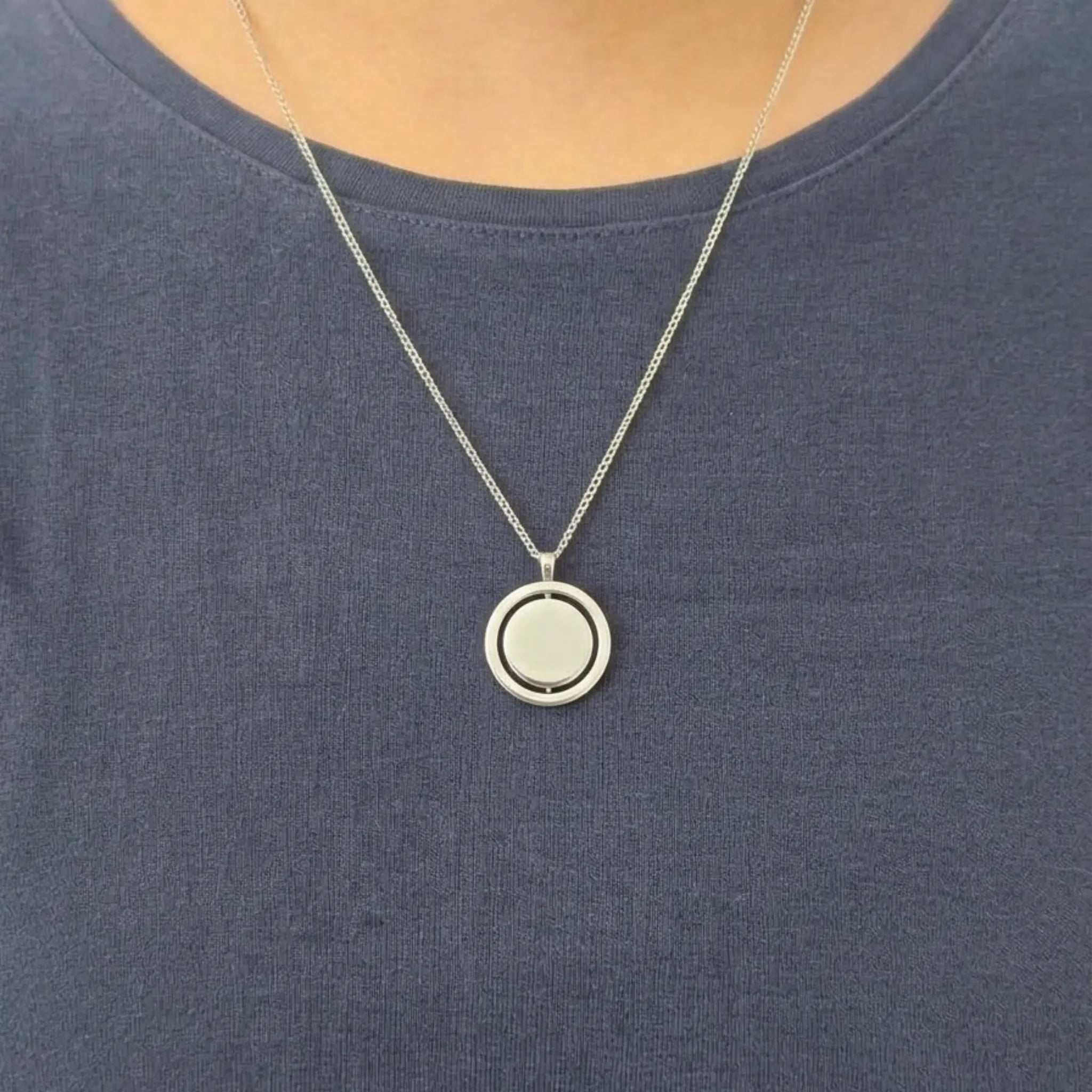 Detailopname van de zilveren Oracle anti-stress ketting van RVS, gedragen door een model in een blauwe top.