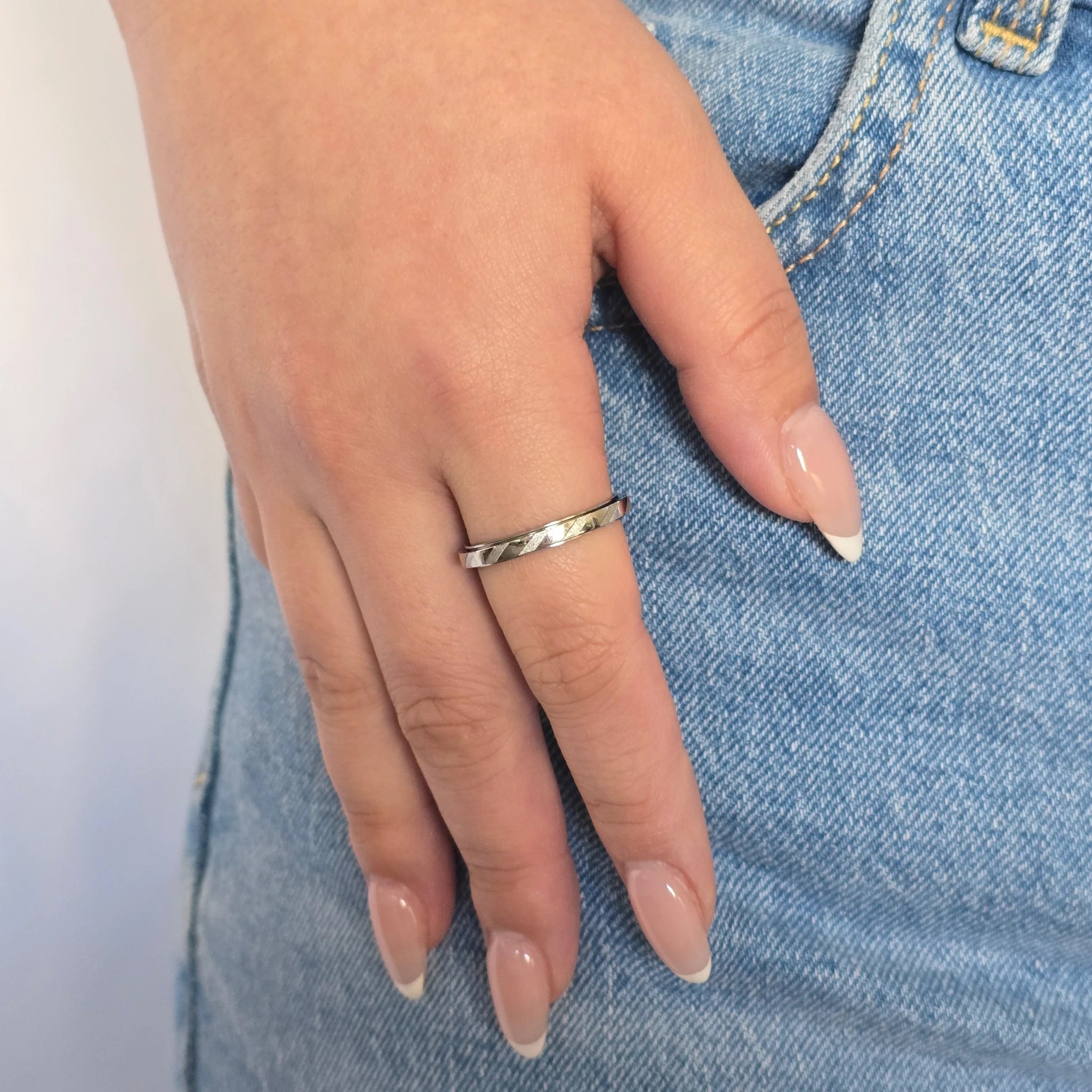 Zilveren Prism anti-stress ring met een subtiel diagonaal patroon, gedragen om de vinger door een vrouw in een blauwe jeans.
