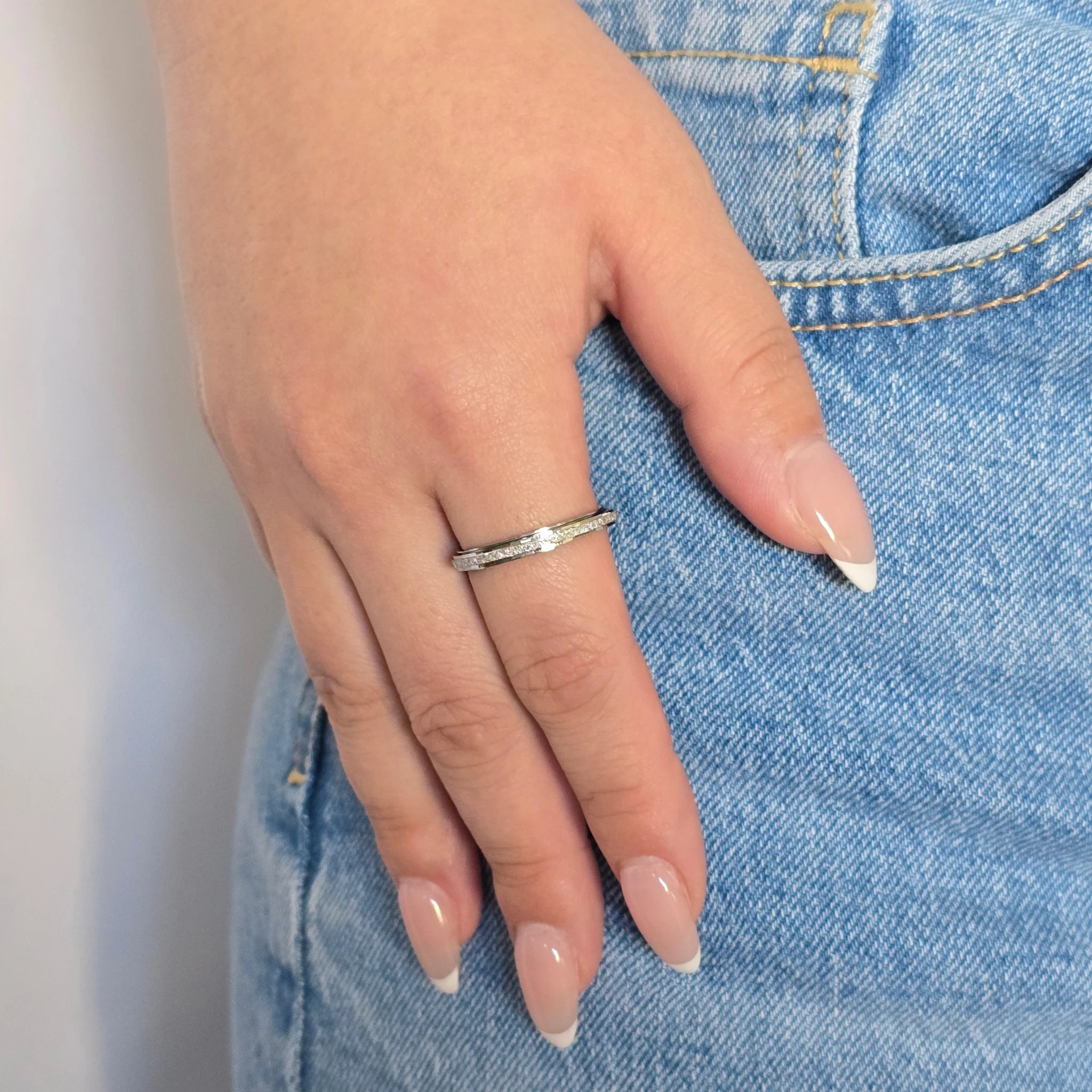 Zilveren anxiety ring gedragen om de wijsvinger door een vrouw in een casual blauwe spijkerbroek.