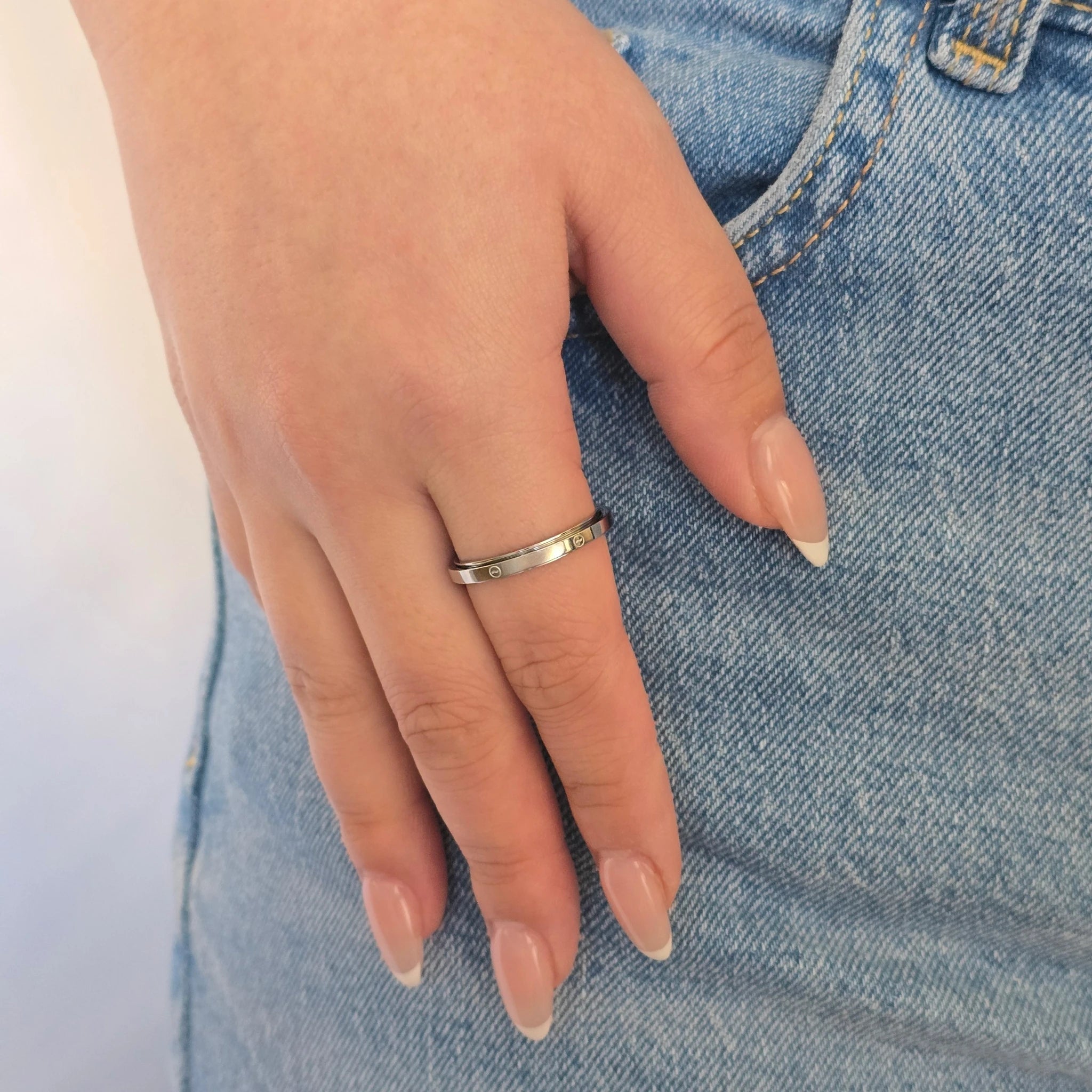 Zilveren anxiety ring met subtiele zeegolf details gedragen om de vinger door een vrouw in een blauwe spijkerbroek.