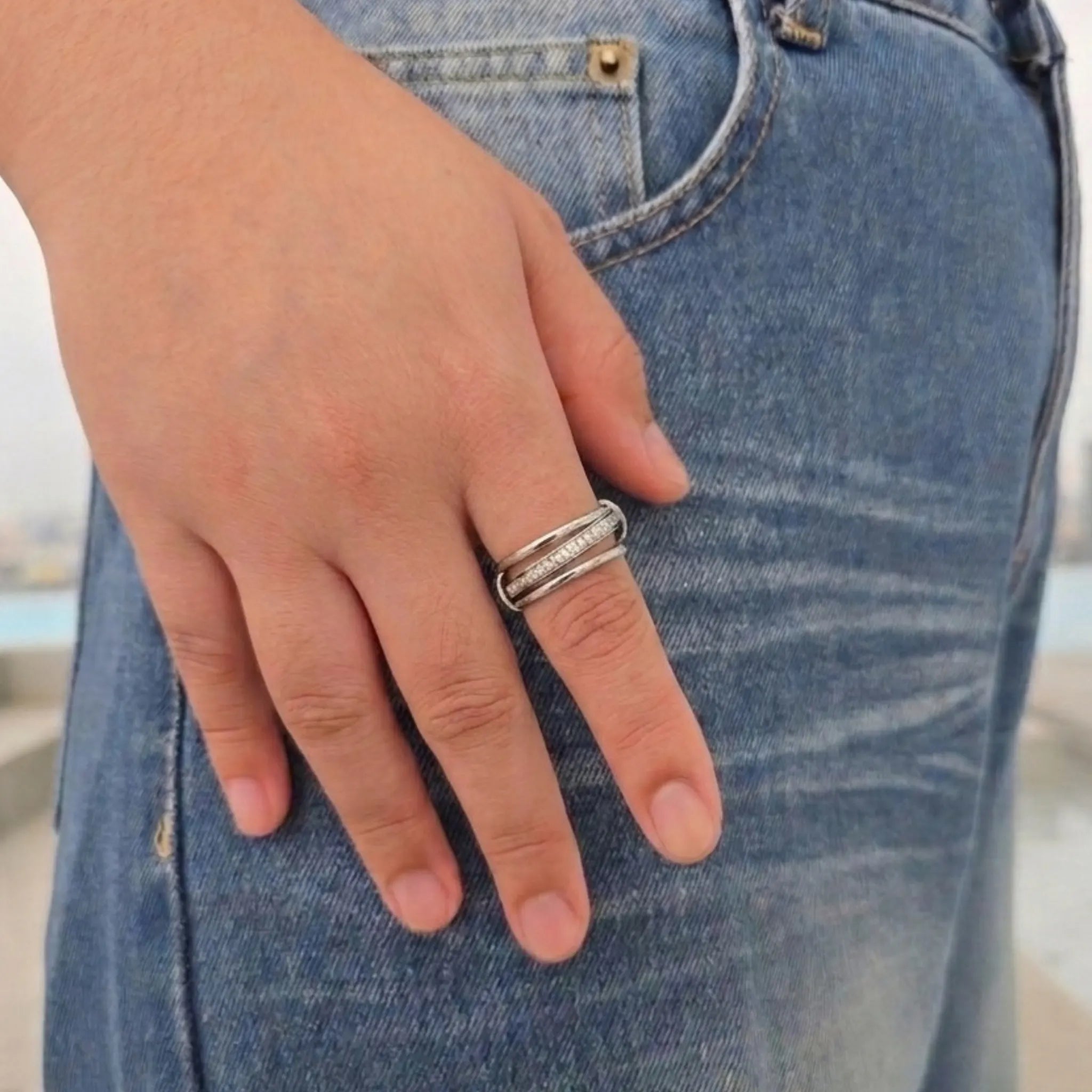 Zilveren Neo anti-stress ring met drie ringen en een draaibare steentjesband om de vinger, gefotografeerd tegen een blauwe spijkerbroek.