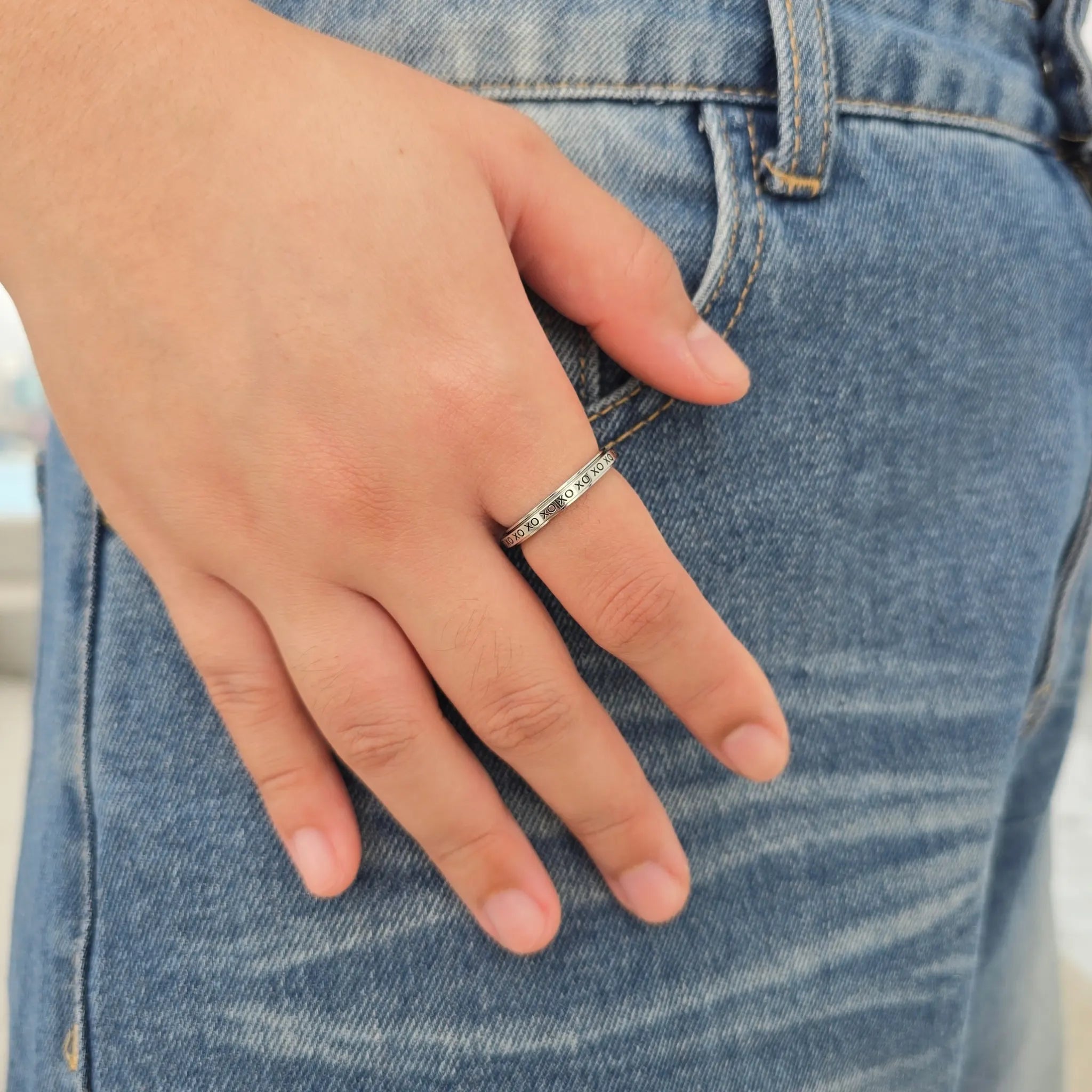 Zilveren XO anti-stress ring van RVS met draaiende XO-inscriptie om de vinger, gefotografeerd tegen een blauwe jeans.